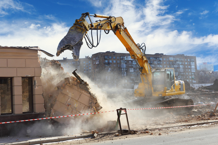 Excavator takes down building safely with ANSI/ASSE A10.6-2006 (R2016) for demolition operations.