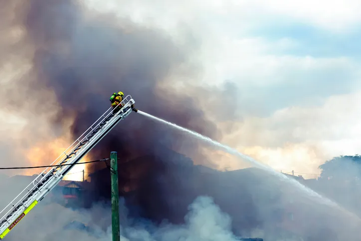 Firefighter on a ladder with water hose trying to control a fire by following NFPA Fire Code 1 2018