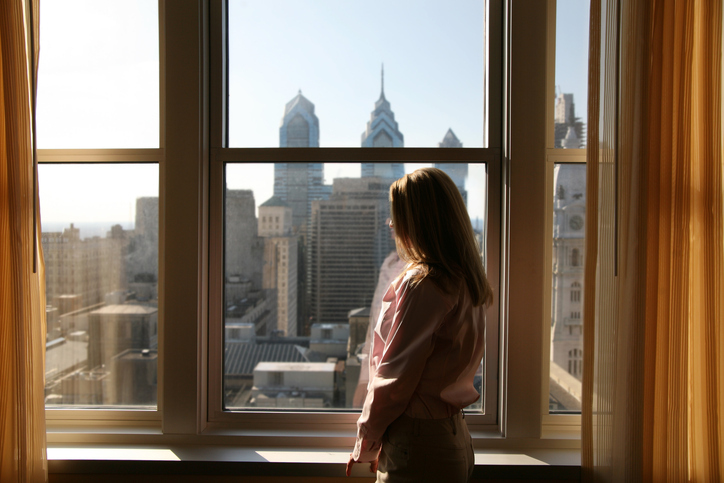 Woman gazing out window at Philadelphia skyline where many follow the North American Fenestration Standard.