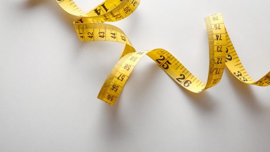 Twisting measuring tape representing the metric system (SI units), which are reflected in standards by an M.