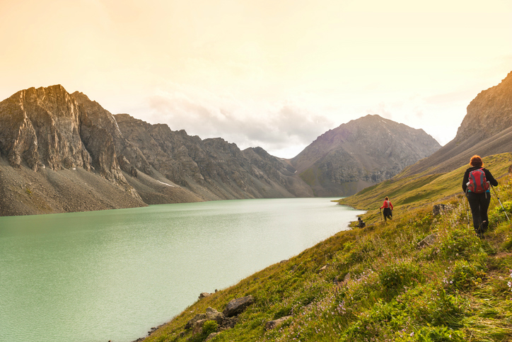 View of a lake within a valley and two hikers walk alongside it, which is symbolic of ISO 9004 2018