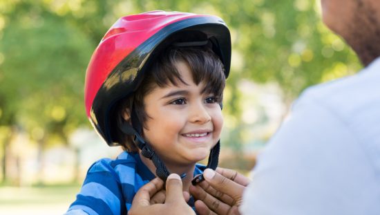 Father tightening red ASTM F1447-18 bicycle helmet on happy son's head.