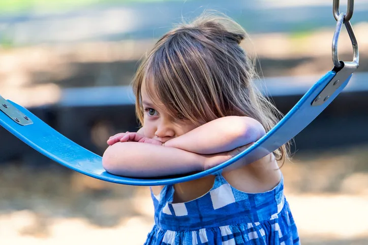 Girl looking sad on swingset, which can be prevented if designed with ASTM F1148-21