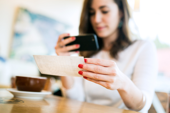 Happy woman in sweater using her cell phone to make a remote deposit to standard.