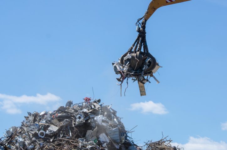 A yellow ASME B30.25-2018 Scrap and material handler in action picking up metal in scrapyard.