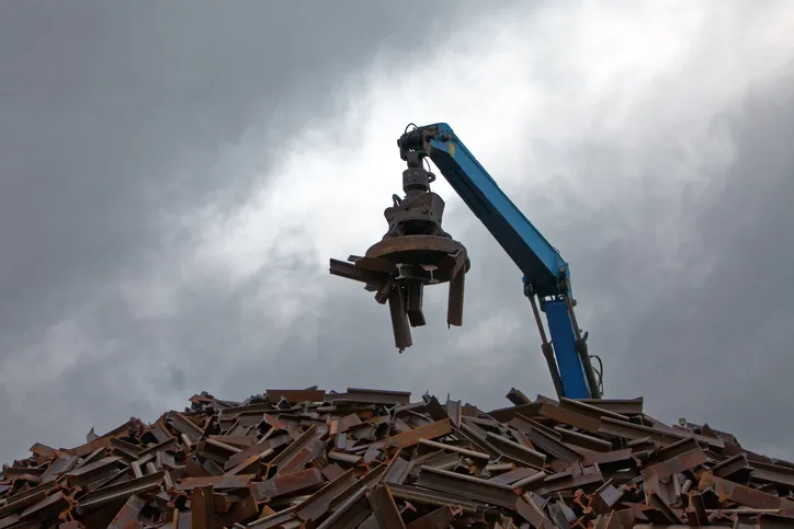 A blue ASME B30.25-2018 machine handling scrap in a junkyard.