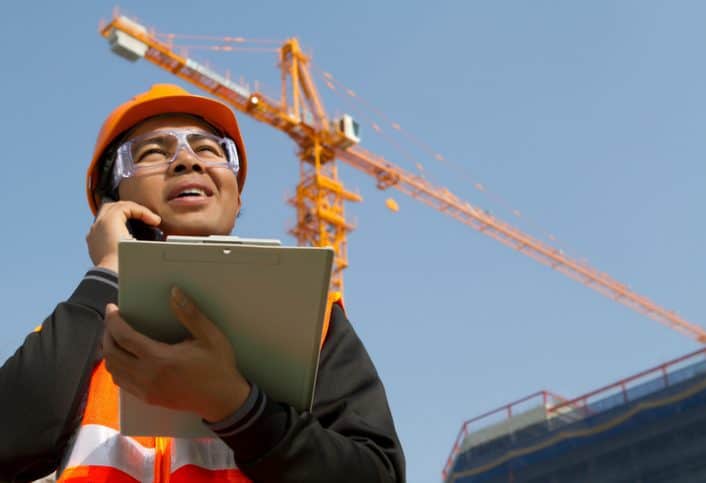Construction site manager holding the ANSI/ASSP A10.28-2018 document and asking about work platforms suspended by cranes.
