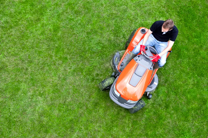 Riding a lawnmower over green grass following ANSI/OPEI B71.10-2018 gasoline fuel systems.