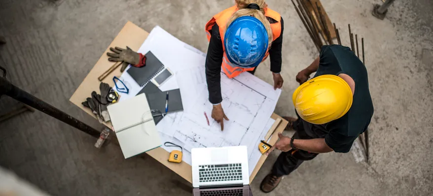 Overhead view of two construction workers discussing over a blueprint