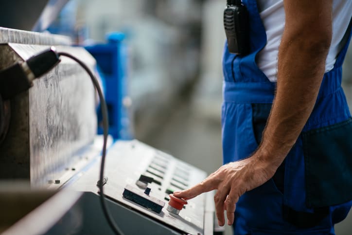 Arbejder er ved at trykke på en advarselsknap på en maskine