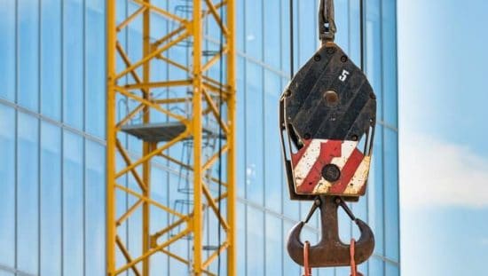 Red and white below-the-hook lifting device in construction site designed to ASME BTH-1-2020.