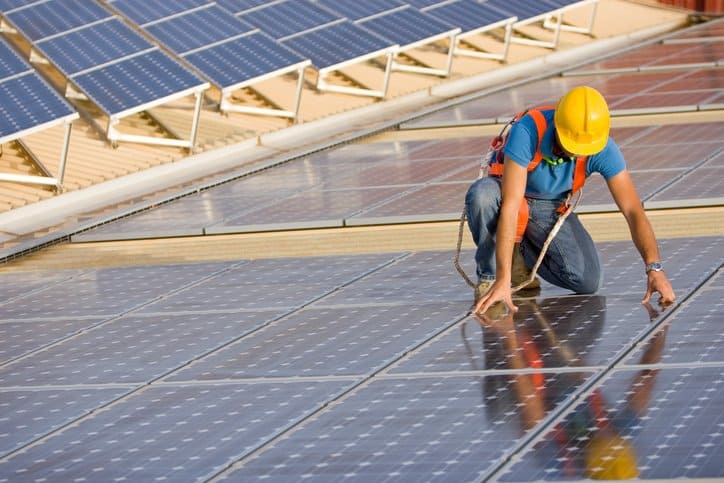 Photovoltaic Installation Worker in hardhat carefully installing solar photovoltaic (PV) panels that will undergo IEEE C57.159-2016 photovoltaic transformers.