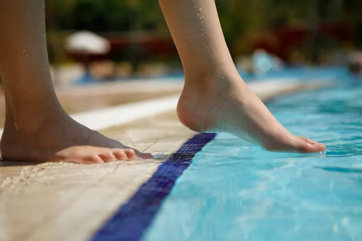 Young girl dipping toe in public pool to test the water quality instead of following ANSI/APSP 11-2019.