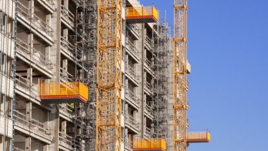 Some yellow ANSI/ASSP A10.5-2020 material hoists carefully installed to transport construction equipment and personnel.