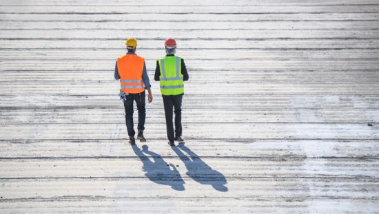 Two construction guys walking on boardwalk from behind and donning ANSI/ISEA 107-2020 high visibility apparel.