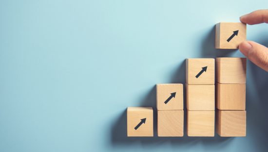 Stacking wood block arrows on blue background to show the quality management progress through ISO 10018:2020 people management.