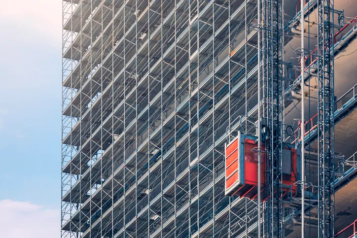 Hoist elevators that follow ANSI/ASSE A10.4-2016 on the side of a building in the process of being constructed.