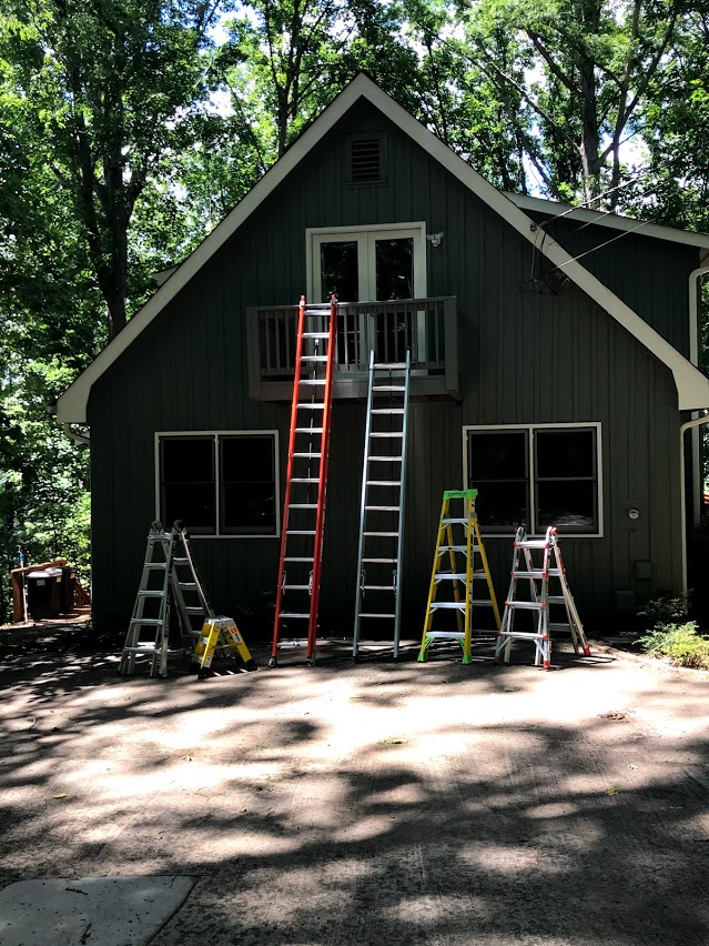 Half dozen colorful ladders safely leaning against small home.