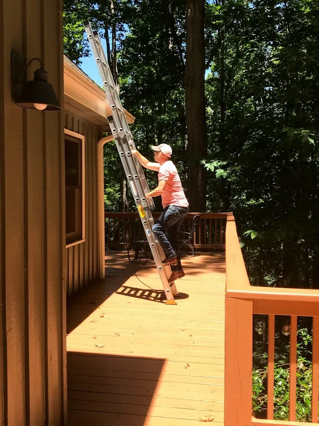 Man climbing ladder at cabin porch using three points of contact.