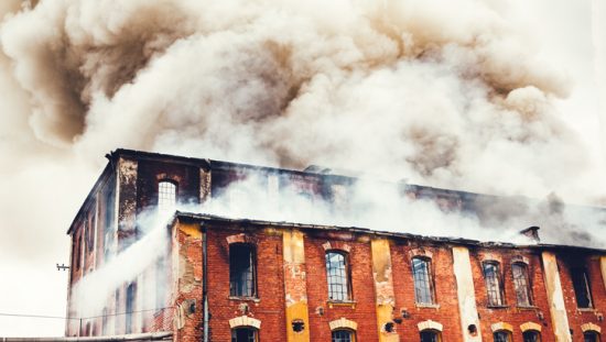 Smoke rising above old brick factory fire that didn't follow the 2021 International Fire Code (ICC IFC-2021).
