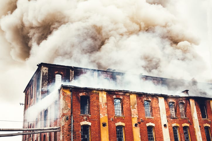Smoke rising above old brick factory fire that didn't follow the 2021 International Fire Code (ICC IFC-2021).