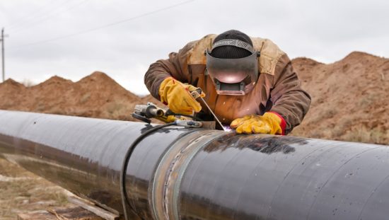Worker covered in PPE in the plains welding a black pipeline with proper ASME B31Q-2021 pipeline personnel qualifications.