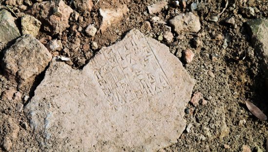 Broken cuneiform tablet in the dirt written in ancient language Akkadian, or in a ISO 639-2 code, akk.