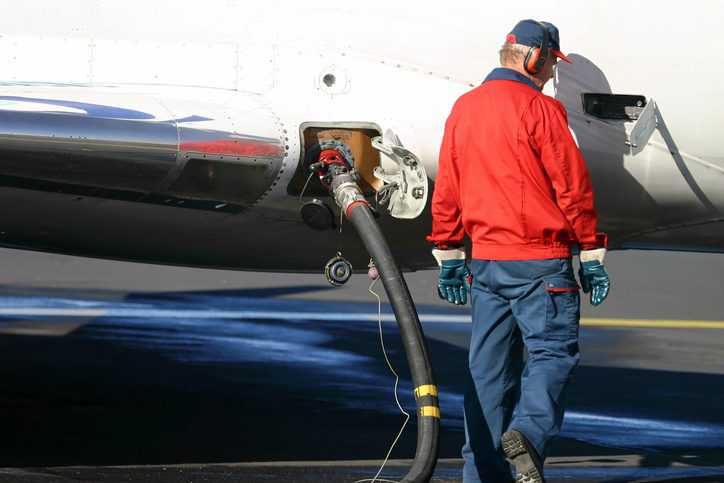 Man in old red windbreaker pumping jet fuel in plane to ASTM D1566-21 specifications.