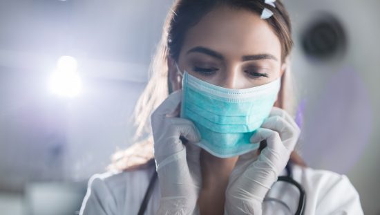 Young female doctor wearing medical face mask adhering to ASTM F2100-21 before surgery.