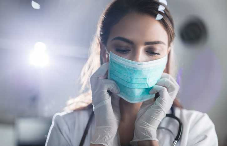 Young female doctor wearing medical face mask adhering to ASTM F2100-21 before surgery.